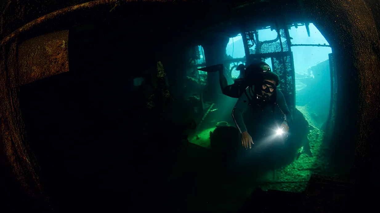 A diver with a torch inside the hold of a wreck